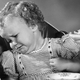 Black and white vintage photo of picky eating toddler, grimacing and turning away from the hand that's trying to feed her with a spoon
